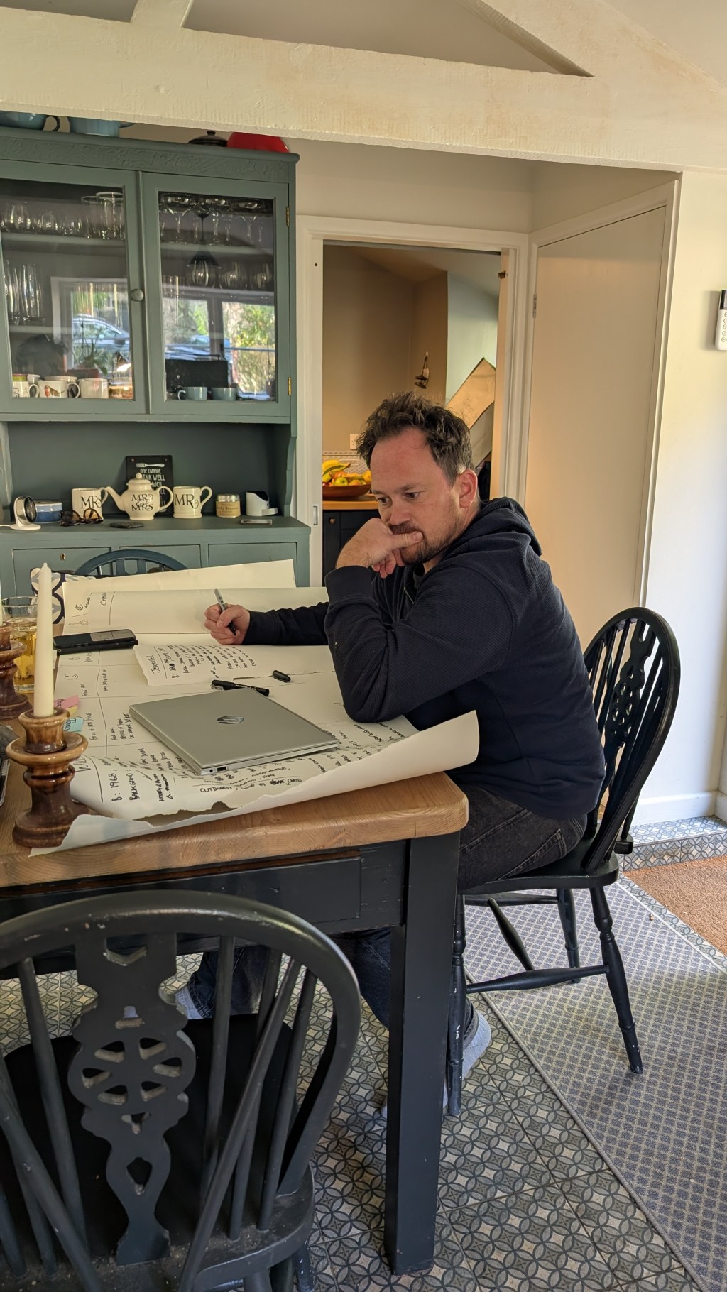 a man at a kitchen table ponders over a large sheet of paper with handwritten ideas